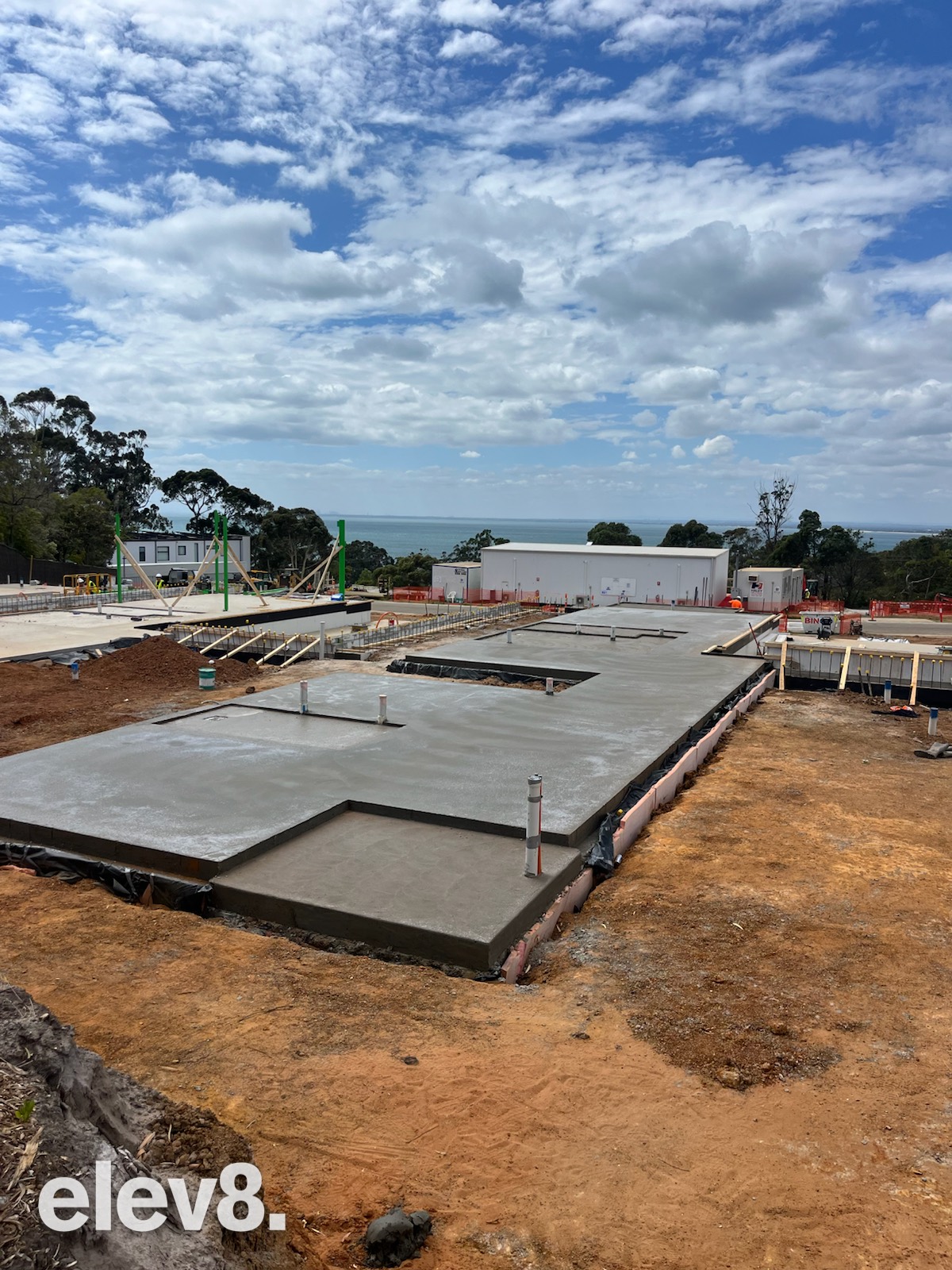 A large house slab, freshly poured, on a sloping block with the bay in the distance