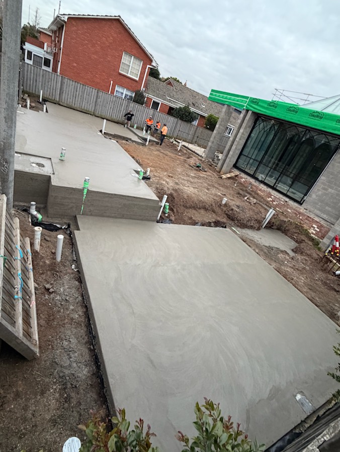 A split-level slab beside a new build, with the crew working in the background